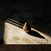 "Brown pear with textured skin cast on a light marble surface, highlighted by soft shadows and warm tones."