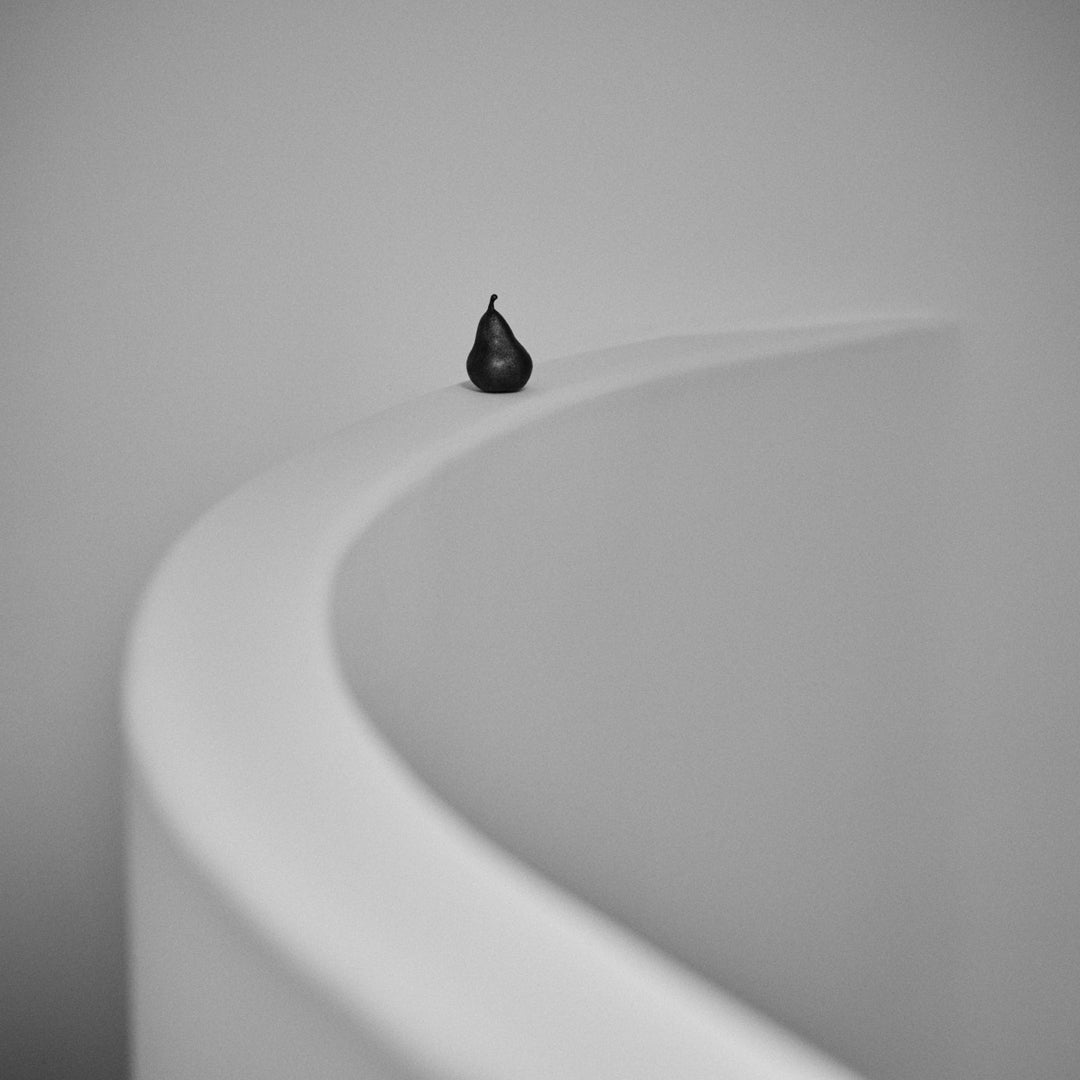 Black pear on a smooth, white, curved surface against a soft grey background. Minimalist and modern aesthetic.