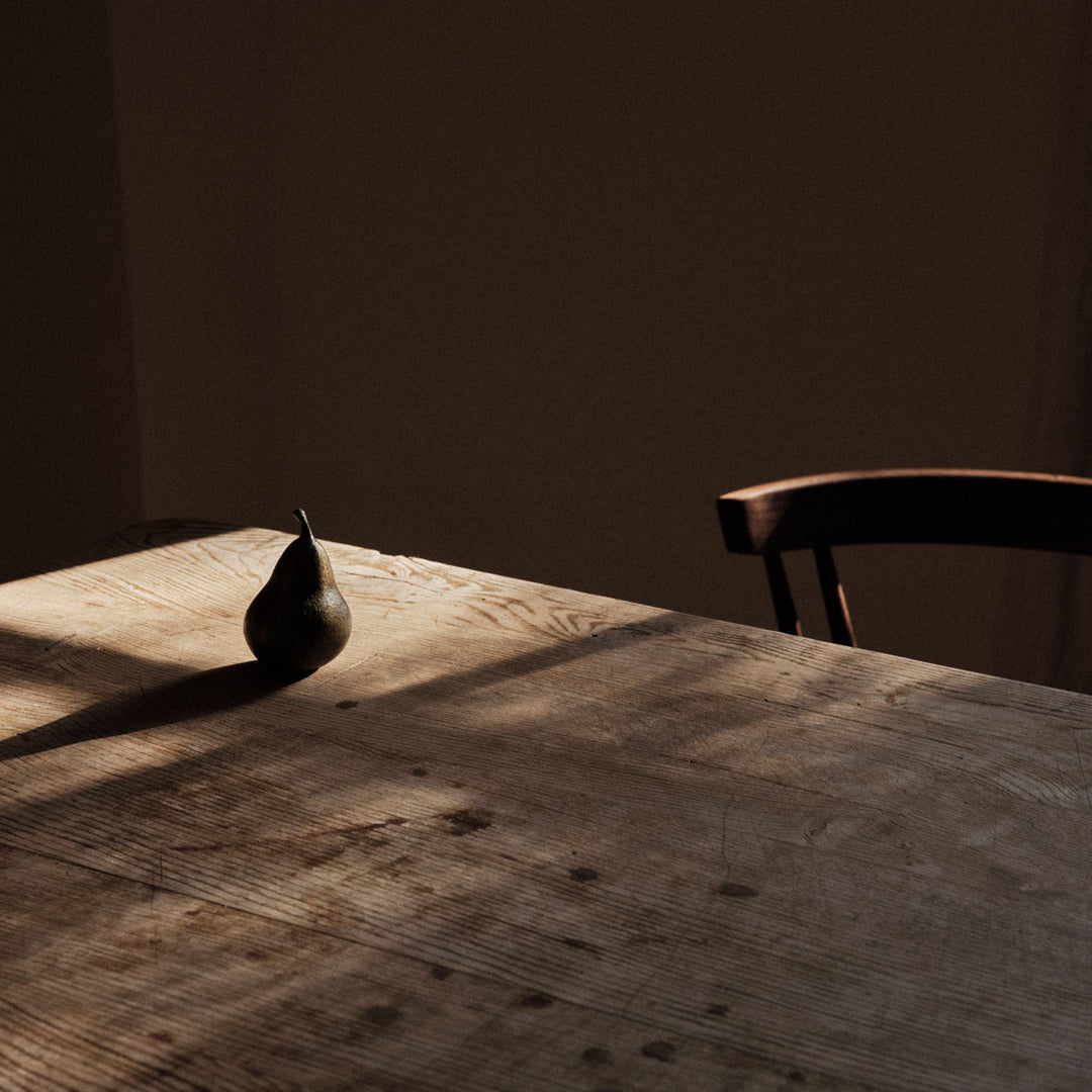 "Dark green pear on a rustic wooden table with warm shadows and a neutral background."