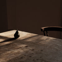 "Dark green pear on a rustic wooden table with warm shadows and a neutral background."