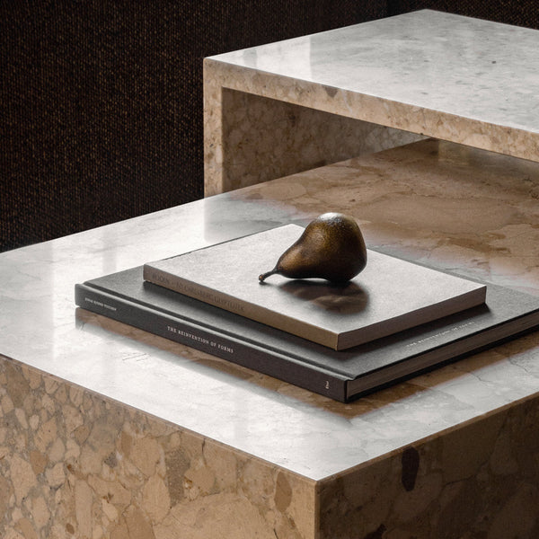 Elegant brown and beige books atop a marble table, with a glossy green pear accent. Sophisticated texture and layering.