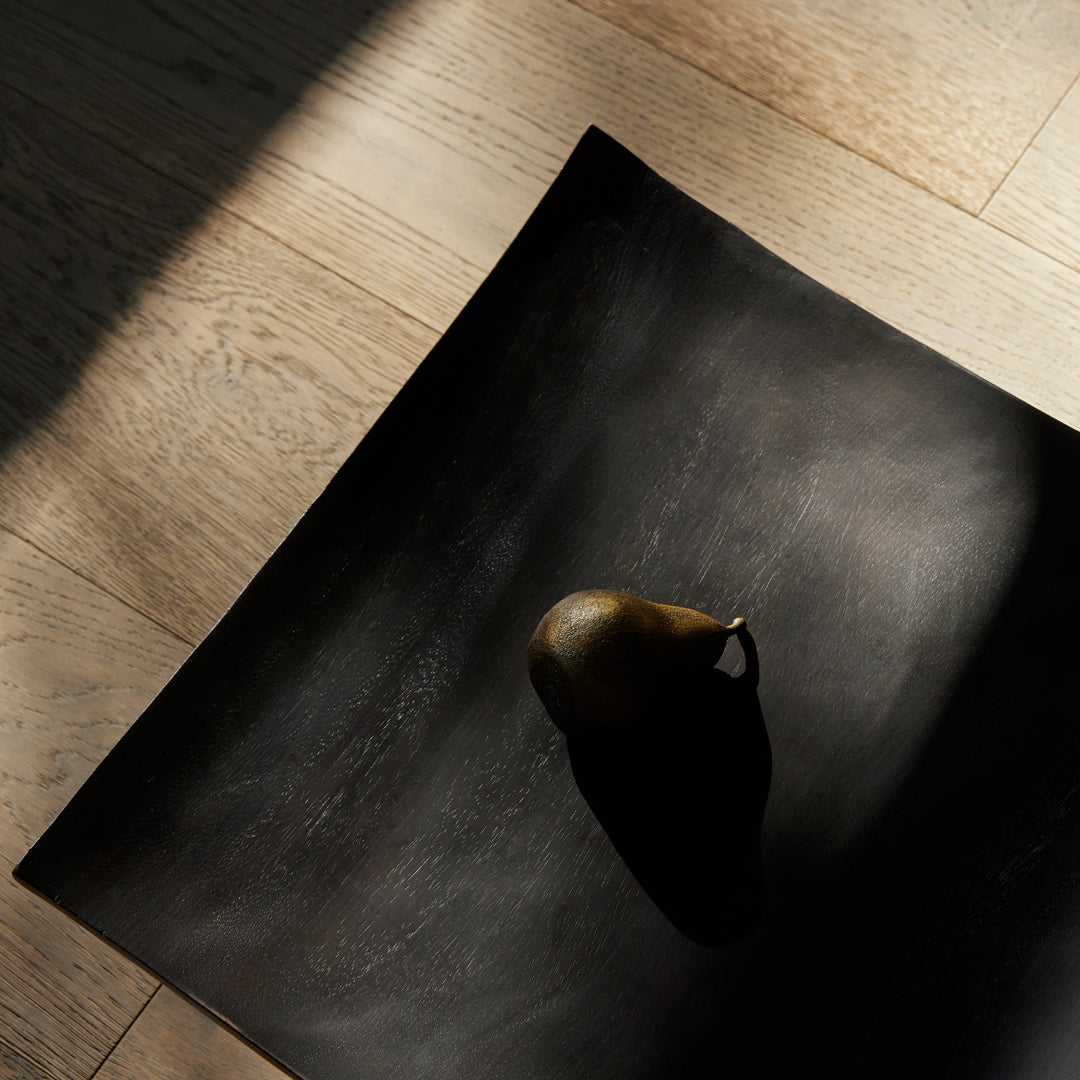 Black textured surface with a shadow, featuring a single greenish-brown pear on a light wooden floor.