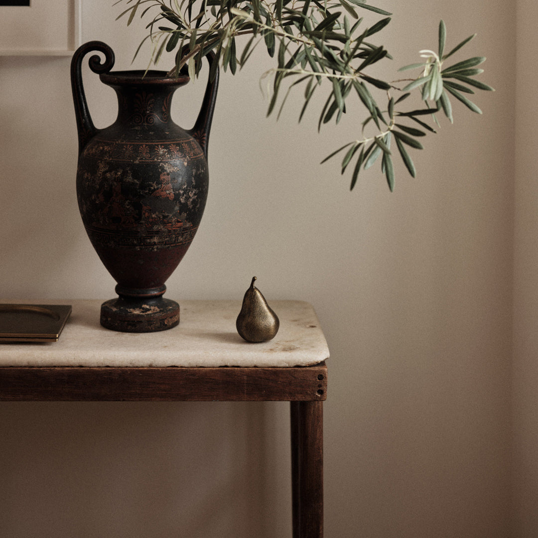Black and red decorative vase with floral patterns, bronze pear accent, and olive greens against a neutral backdrop.