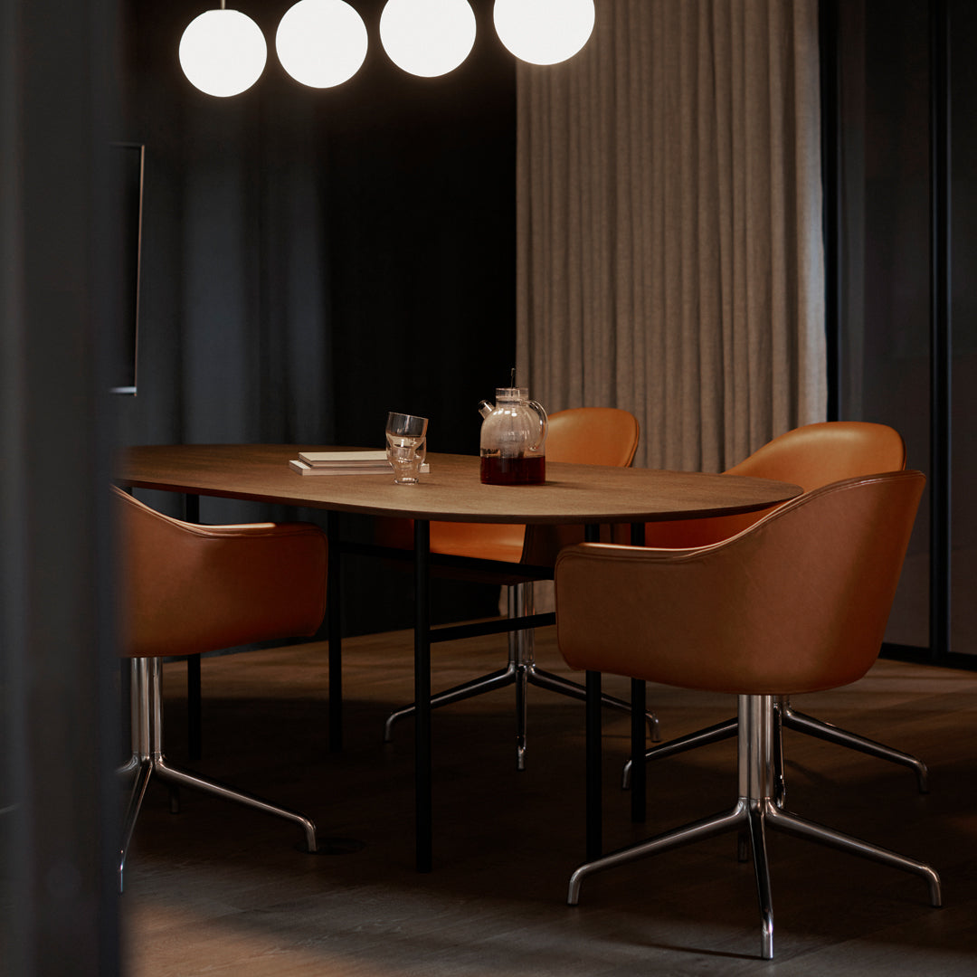 Modern dining table with warm brown leather chairs, sleek black legs, and soft beige curtains against a dark backdrop.