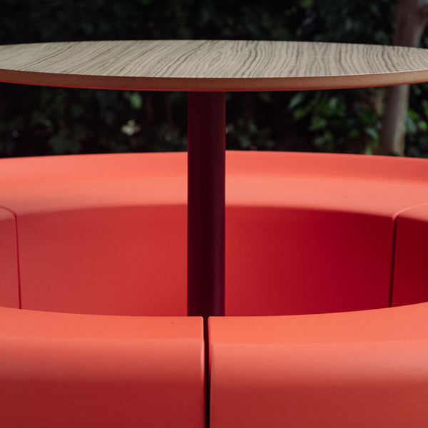 Modern round table with a wood finish, surrounded by bold orange cushion seating pattern.
