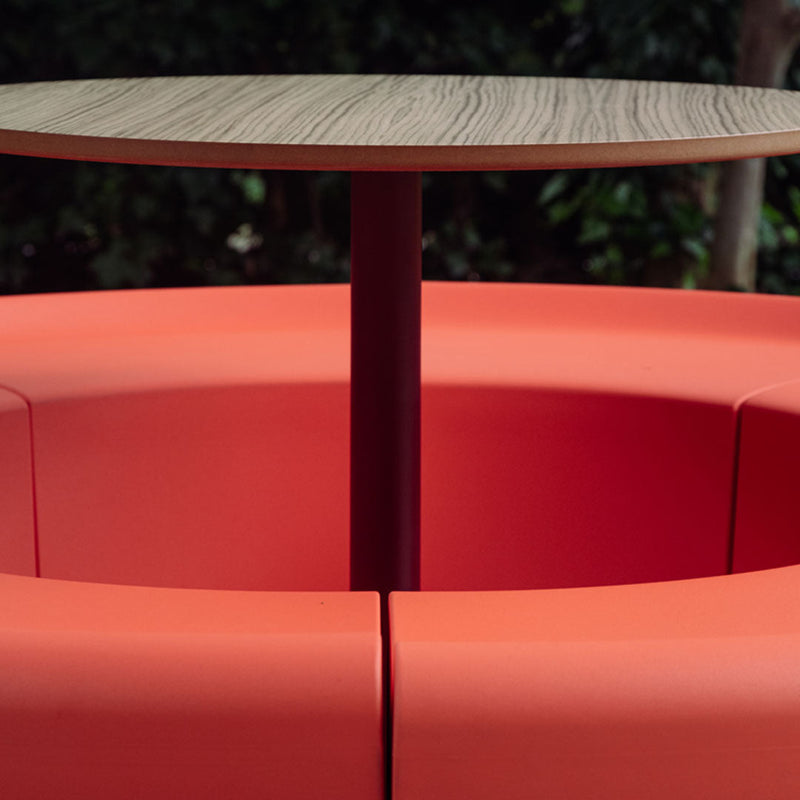 Modern round table with a wood finish, surrounded by bold orange cushion seating pattern.
