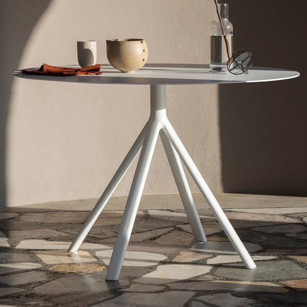 Modern round table with a sleek white finish and unique tripod base, set against a textured stone floor.