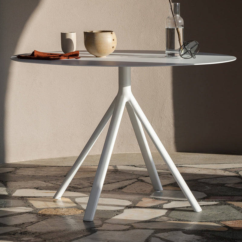 Modern round table with a sleek white finish and unique tripod base, set against a textured stone floor.