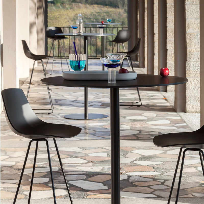 Modern outdoor dining set featuring black chairs and a sleek round table on a textured stone patio.