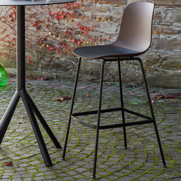 Modern dark gray bar stool with smooth contours and black metal legs, set against a cobblestone background.