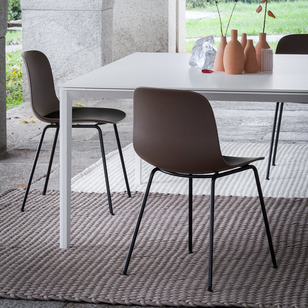 Brown chairs with black legs on a textured light gray woven rug, paired with a minimalist white table and pastel ceramic vases.