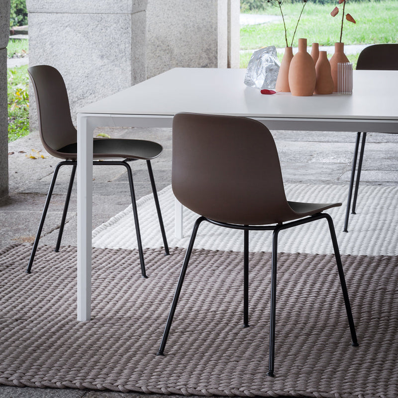 Brown chairs with black legs on a textured light gray woven rug, paired with a minimalist white table and pastel ceramic vases.