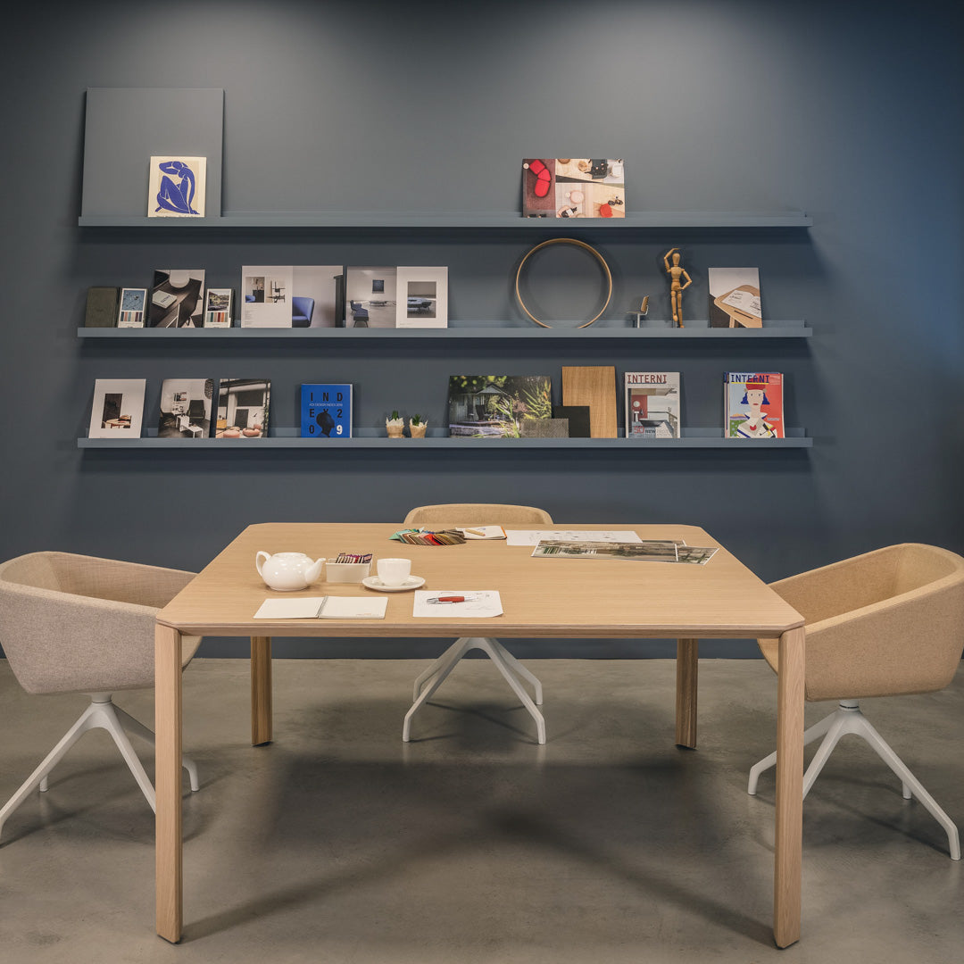 Modern pastel chairs and a light wood table against a deep blue wall with white shelves and colorful art.