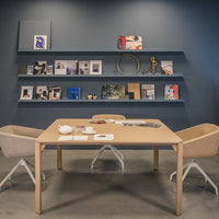 Modern pastel chairs and a light wood table against a deep blue wall with white shelves and colorful art.