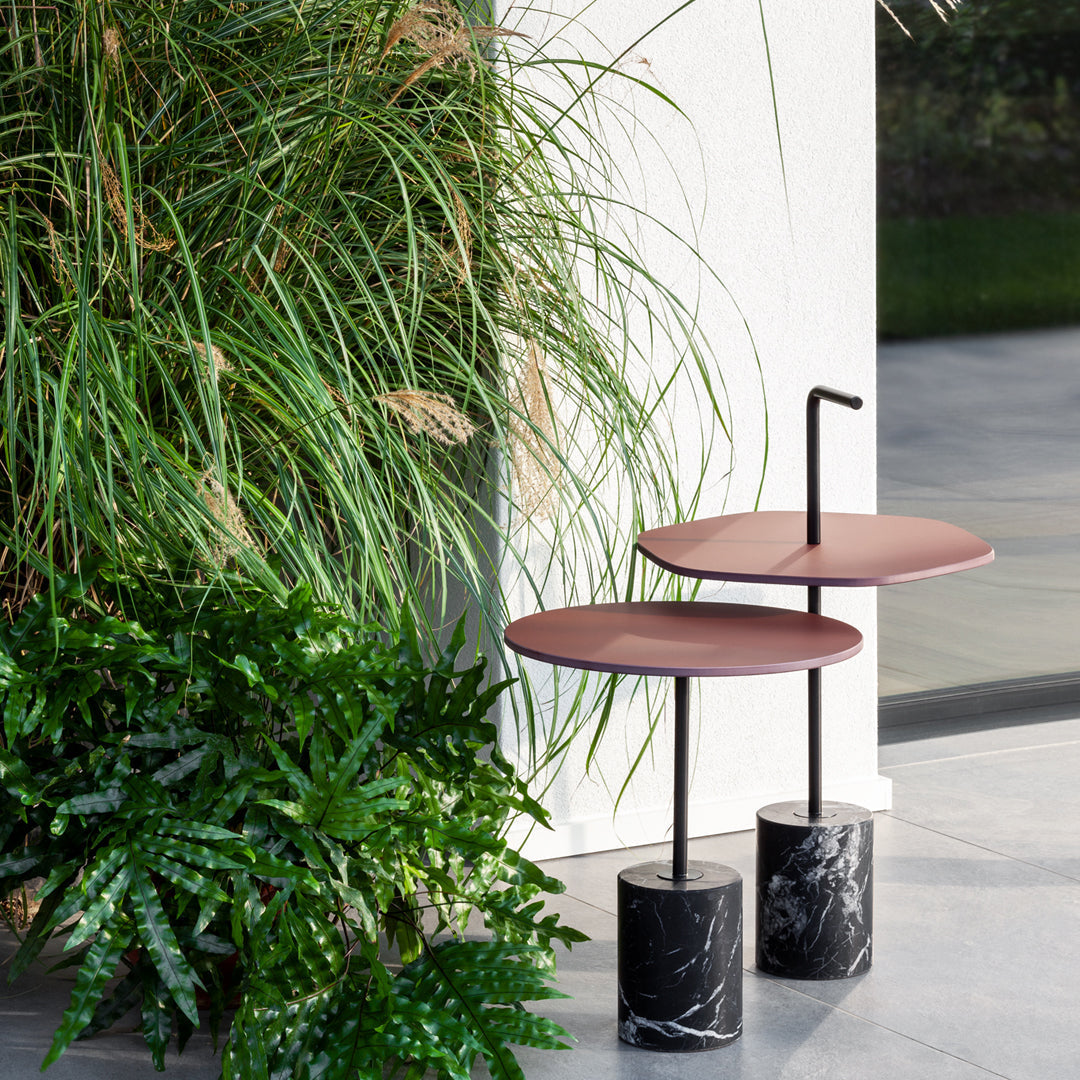 Modern side tables featuring soft maroon tops and sleek black marble bases, complemented by lush greenery.