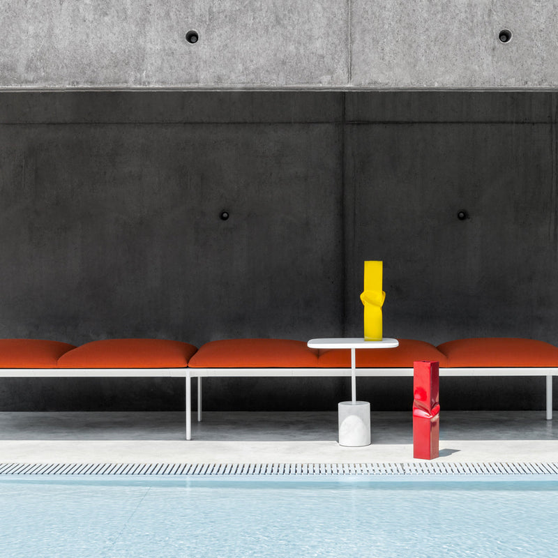 Orange cushions on a modern white bench, complemented by bright yellow and red accents against a gray background.
