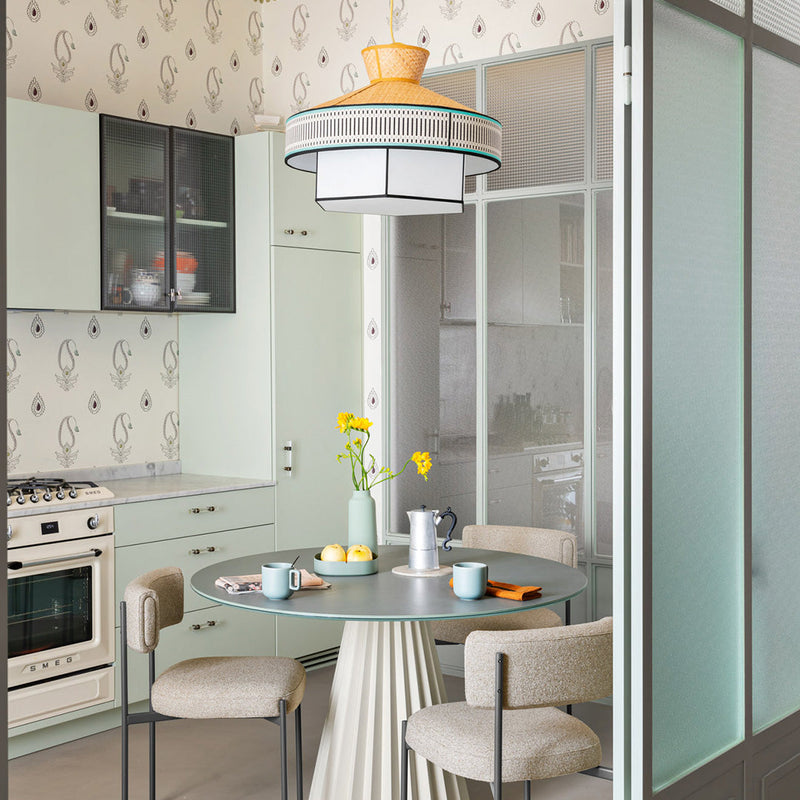Light green cabinetry with floral wallpaper, soft gray table, and warm orange pendant lamp in a modern kitchen setting.