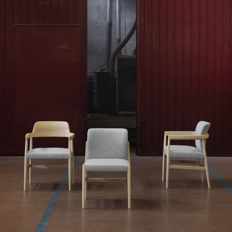 "Set of three modern chairs in light wood, featuring gray and white upholstery against a dark industrial backdrop."