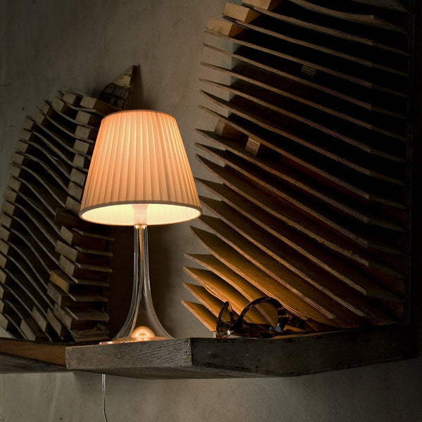 Elegant beige lamp with a ribbed shade, set against a textured wooden background in a warm, subdued color palette.