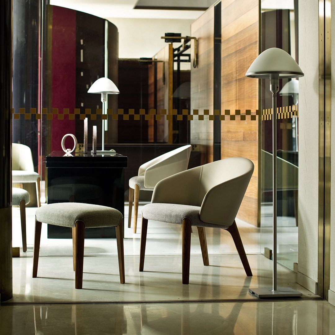 Modern beige chairs with wooden legs, set against dark wood panels and sleek glass elements for a contemporary look.