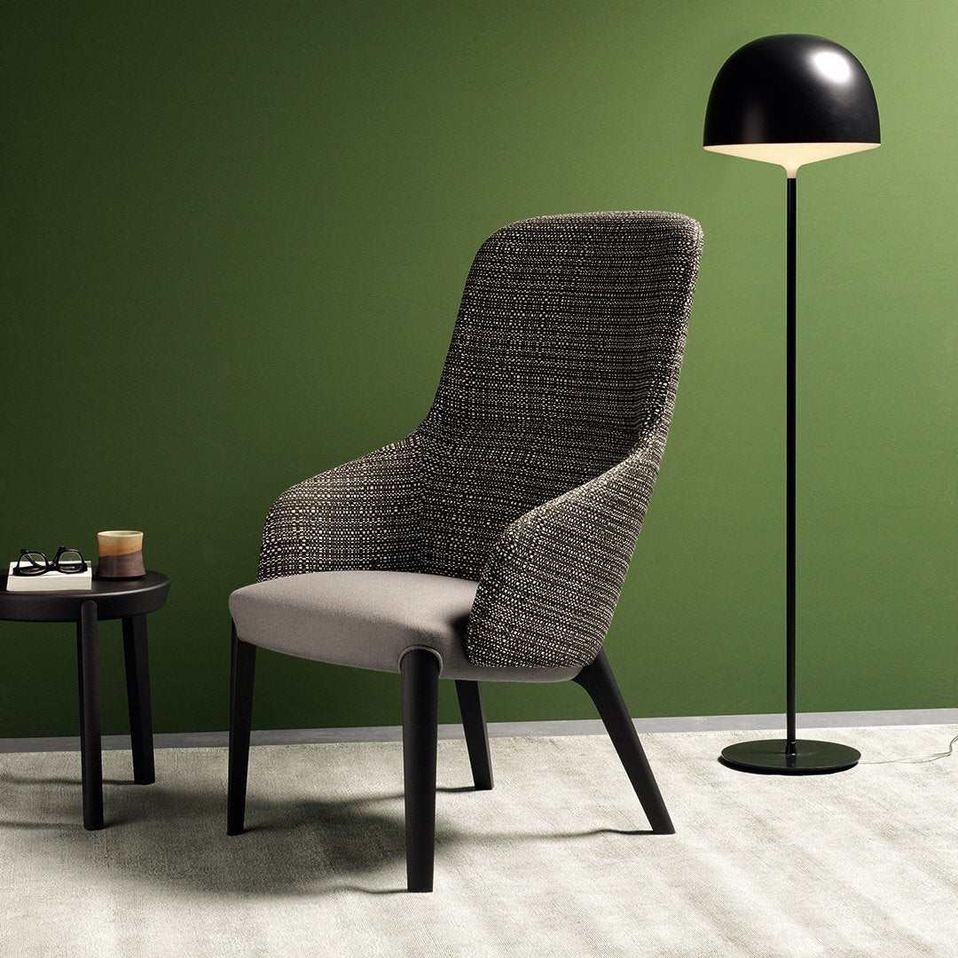 Stylish gray woven chair with black legs, set against a deep green wall, complemented by a sleek black floor lamp.
