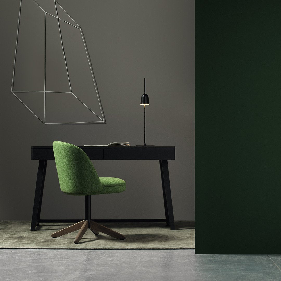 Green upholstered chair against black desk and dark green wall; minimalist design highlighted by geometric lines.
