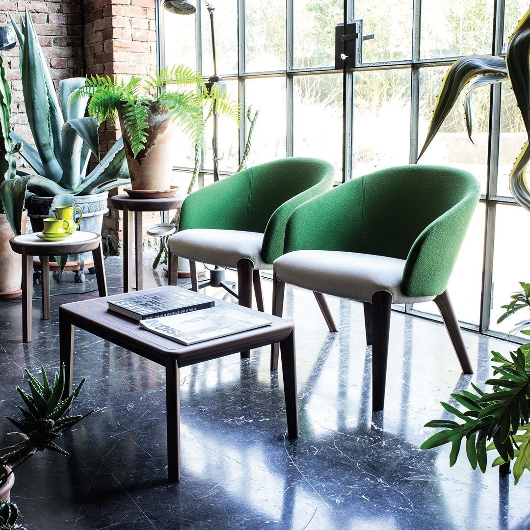 Green and white upholstered chairs with wooden legs, set on a dark marble floor amidst lush indoor plants.