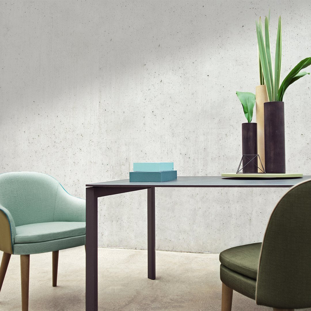 Modern table with sleek black legs, paired with mint green and dark green chairs against a minimalist concrete backdrop.