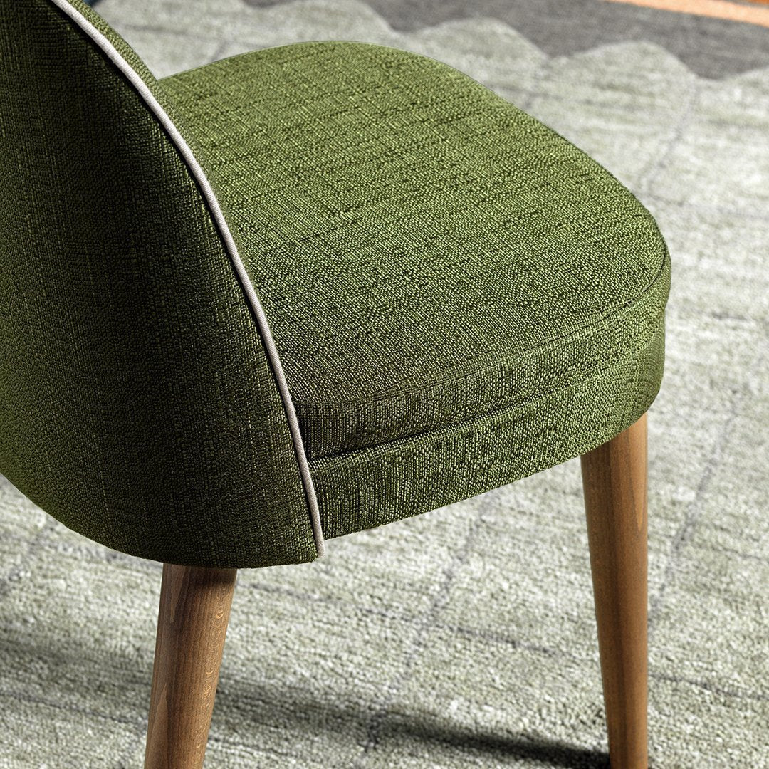 Green textured chair fabric with light stitching, complemented by natural wooden legs against a patterned gray rug.