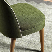 Green textured chair fabric with light stitching, complemented by natural wooden legs against a patterned gray rug.