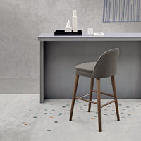 Stylish gray bar stool with wooden legs, set against a minimalist concrete background and patterned floor.