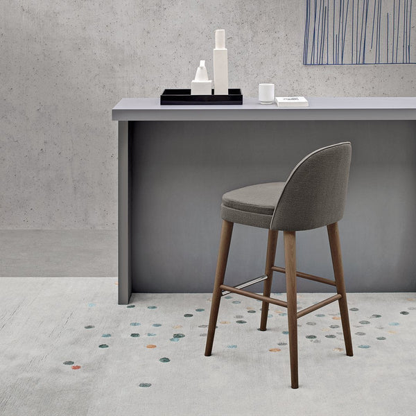 Stylish gray bar stool with wooden legs, set against a minimalist concrete background and patterned floor.