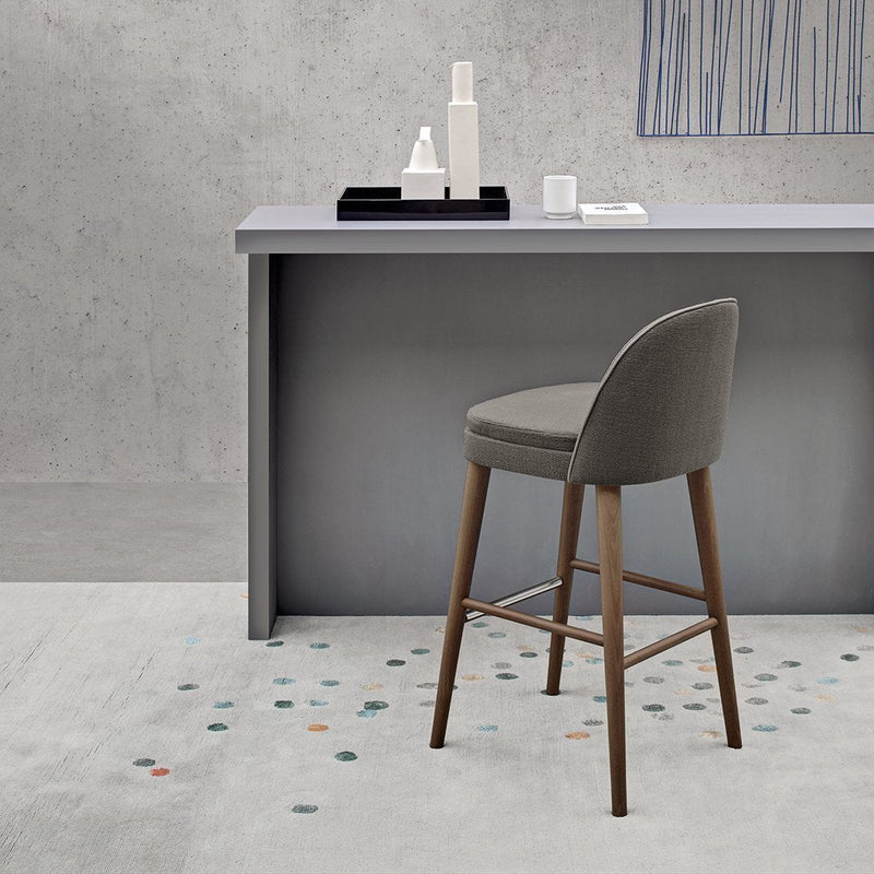 Stylish gray bar stool with wooden legs, set against a minimalist concrete background and patterned floor.