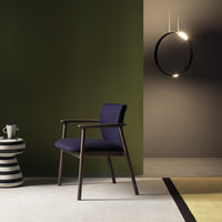 Purple upholstered chair with a dark wood frame, set against green and neutral walls, featuring striped and geometric patterns on the floor.