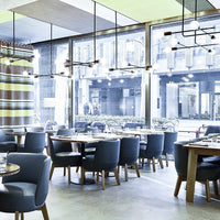 Modern restaurant interior featuring gray-blue chairs, wooden tables, and striped curtains in muted colors.