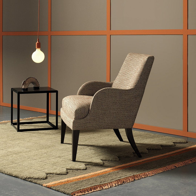 Textured beige chair on a geometric patterned rug, surrounded by neutral tones and orange accents.