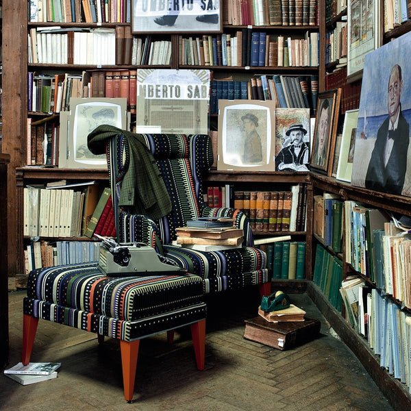 Colorful striped armchair with a mix of blue, red, and green patterns, set against a rustic wooden library backdrop.