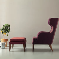 Plush purple armchair with matching ottoman, featuring sleek wooden legs and a minimalist design against a neutral backdrop.