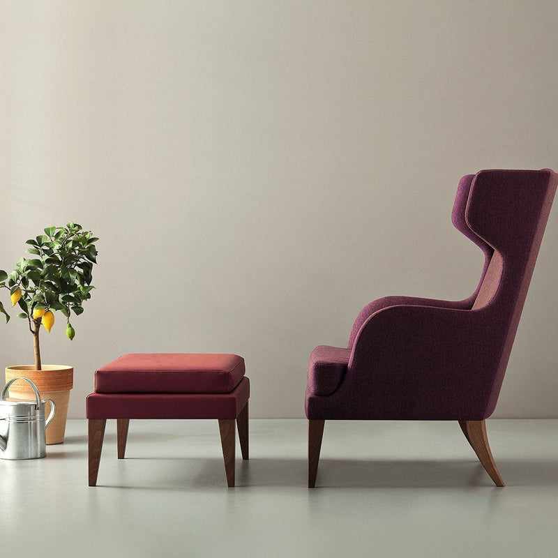 Plush purple armchair with matching ottoman, featuring sleek wooden legs and a minimalist design against a neutral backdrop.