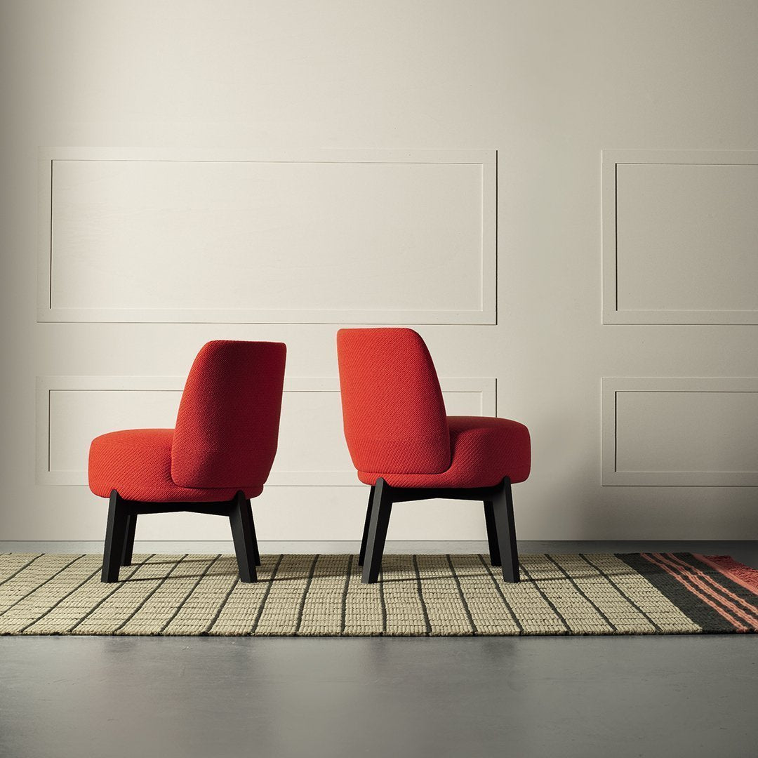 Red upholstered chairs with black legs, positioned on a patterned rug with earthy tones and geometric lines.