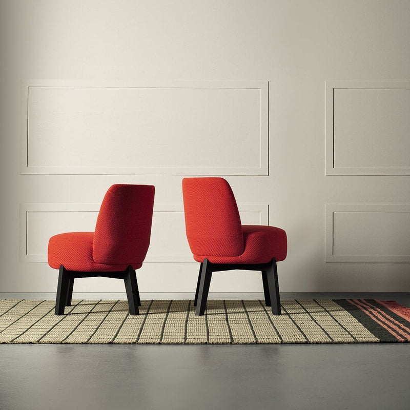 Red upholstered chairs with black legs, positioned on a patterned rug with earthy tones and geometric lines.