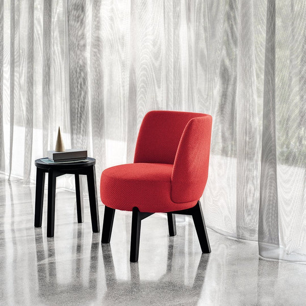 Vibrant red upholstered chair with smooth curves, paired with a sleek black side table, set against sheer curtains.