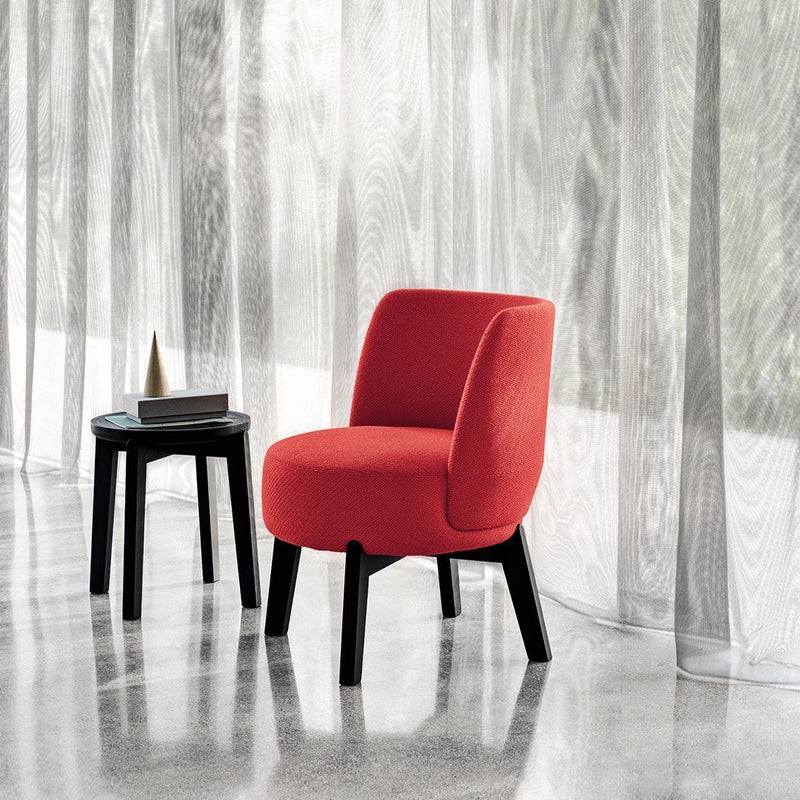 Vibrant red upholstered chair with smooth curves, paired with a sleek black side table, set against sheer curtains.