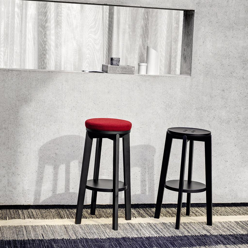 Black bar stools with red and black cushions, set against a textured gray wall and striped patterned rug.