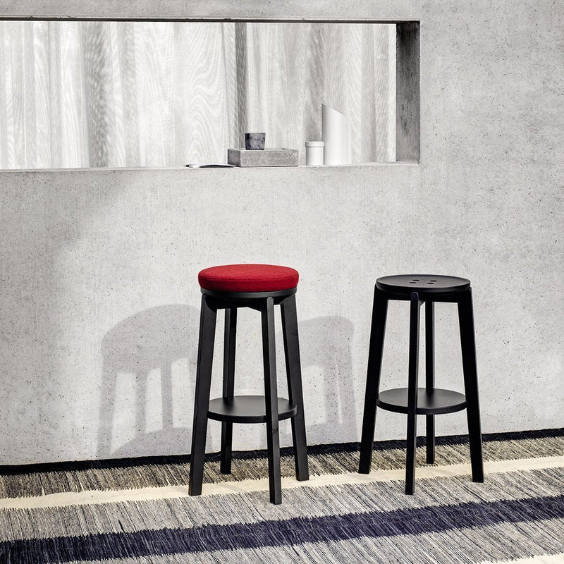 Two modern bar stools with a red upholstered seat and sleek black wooden legs, set against a neutral backdrop.