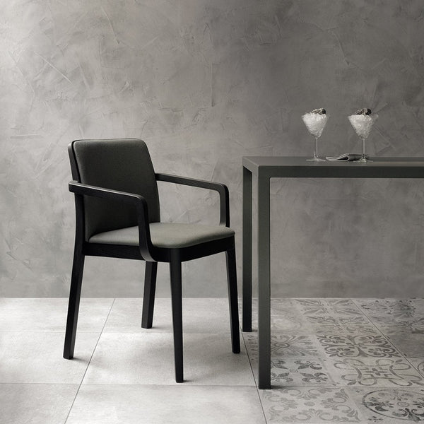 Black chair with gray cushions beside a sleek gray table; patterned floor tiles in light and dark tones.