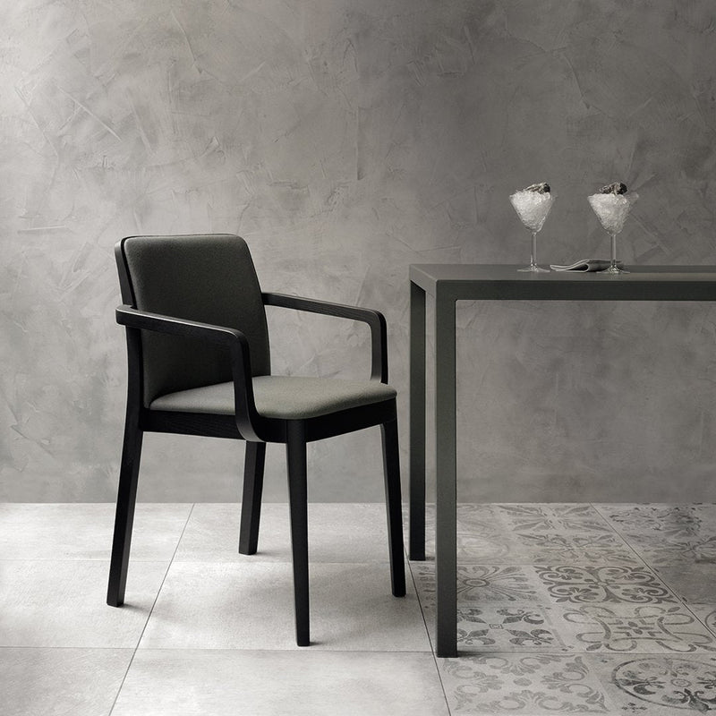 Black chair with gray cushions beside a sleek gray table; patterned floor tiles in light and dark tones.