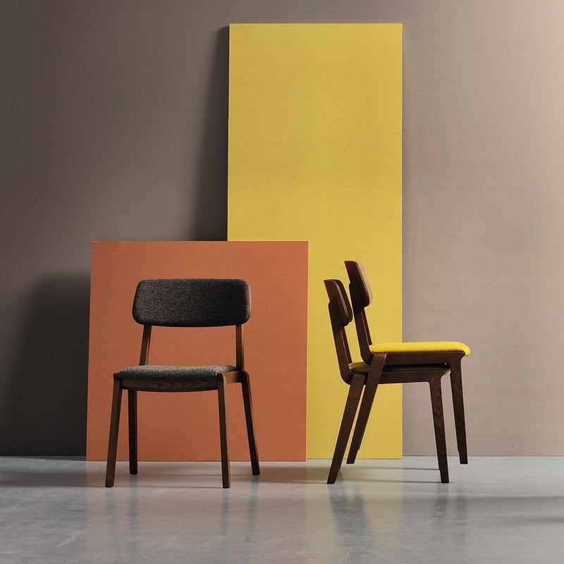 "Two stylish chairs: one in dark gray and one in vibrant yellow, against colorful geometric backdrops of brown and yellow."