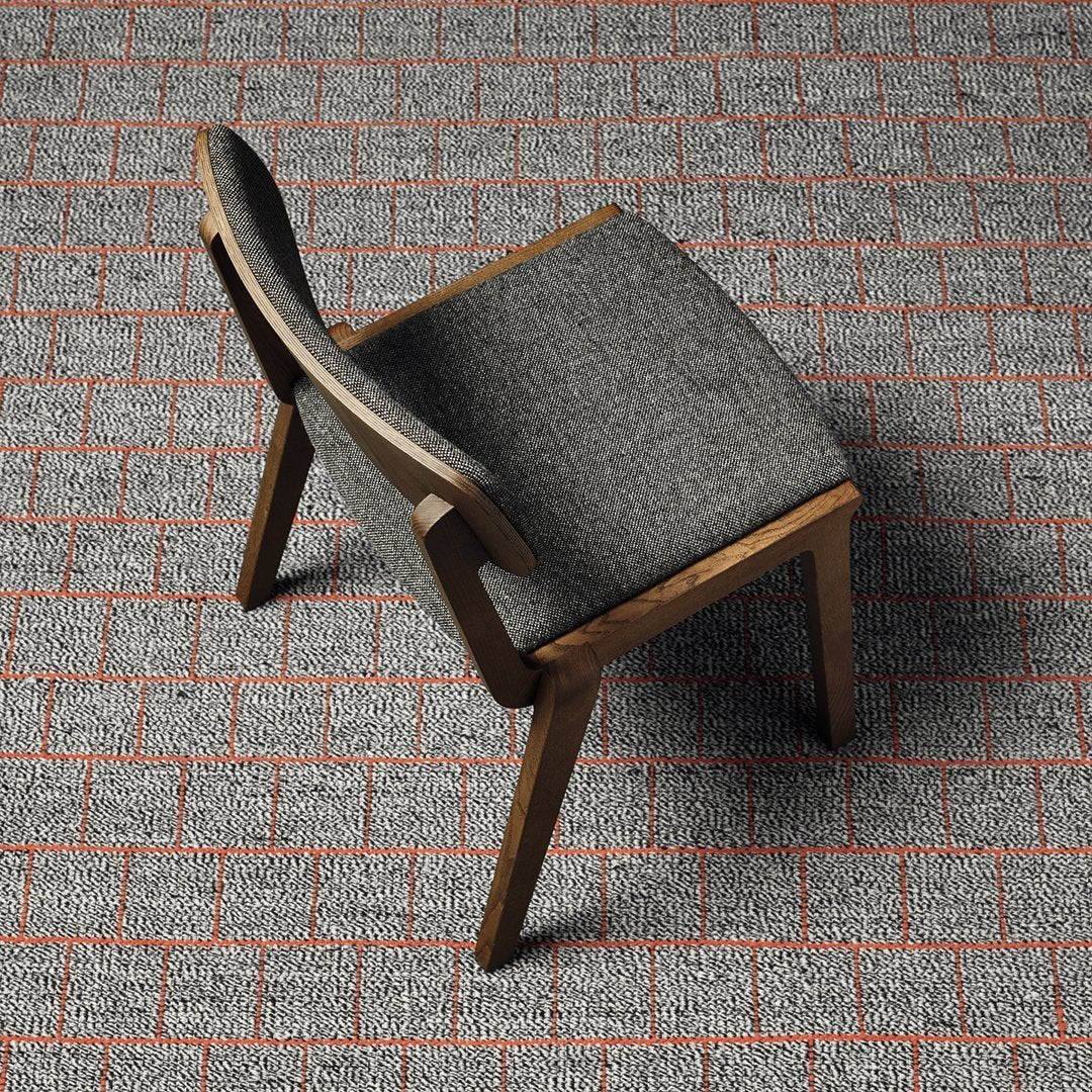 Gray upholstered chair with wood legs on a textured red brick-patterned floor.