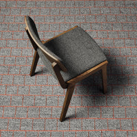 Gray upholstered chair with wood legs on a textured red brick-patterned floor.